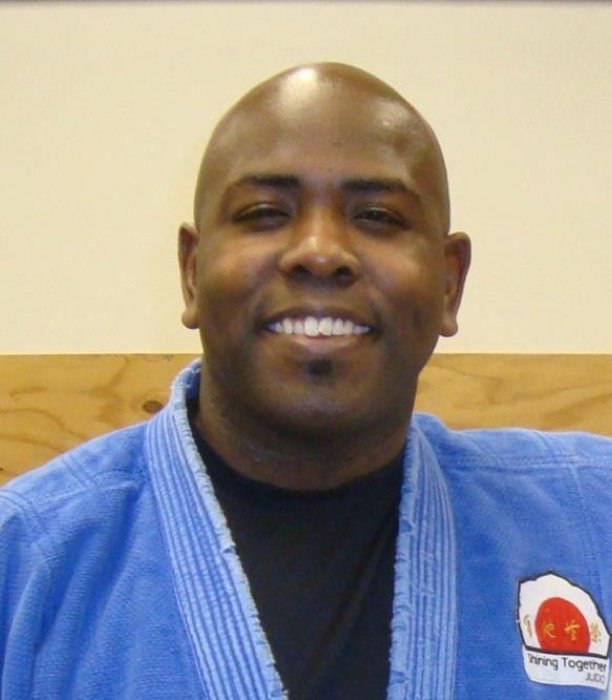 Coach Dennis McCarter smiling in a blue judogi