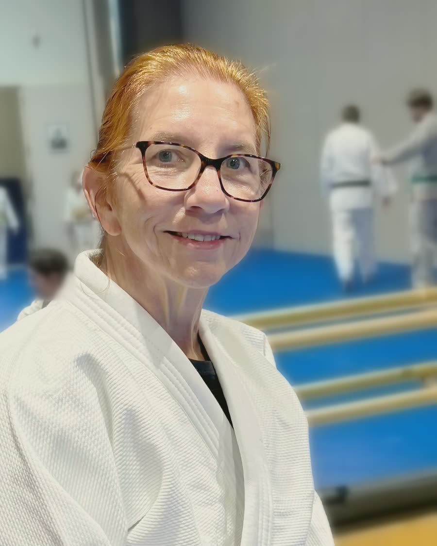 Kristina Baker smiling in a white judogi beside the mat at Finley Center