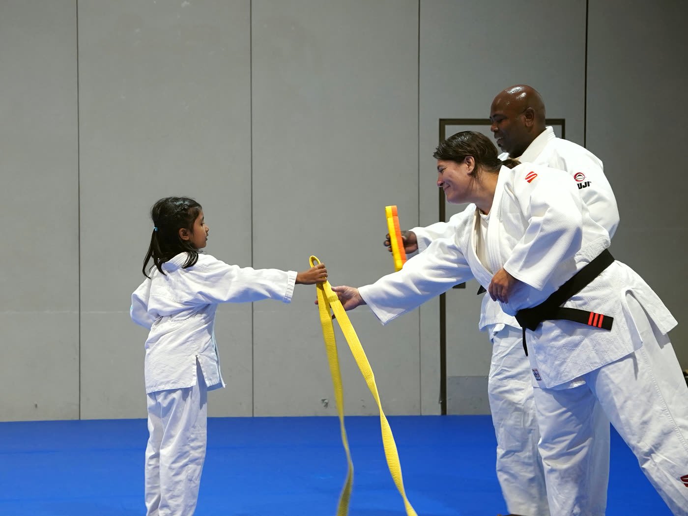 A coach hands a young girl her new yellow belt at promotion night
