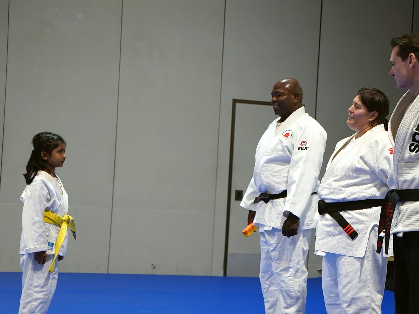 A young student stands facing a line of black-belt coaches at promotion night
