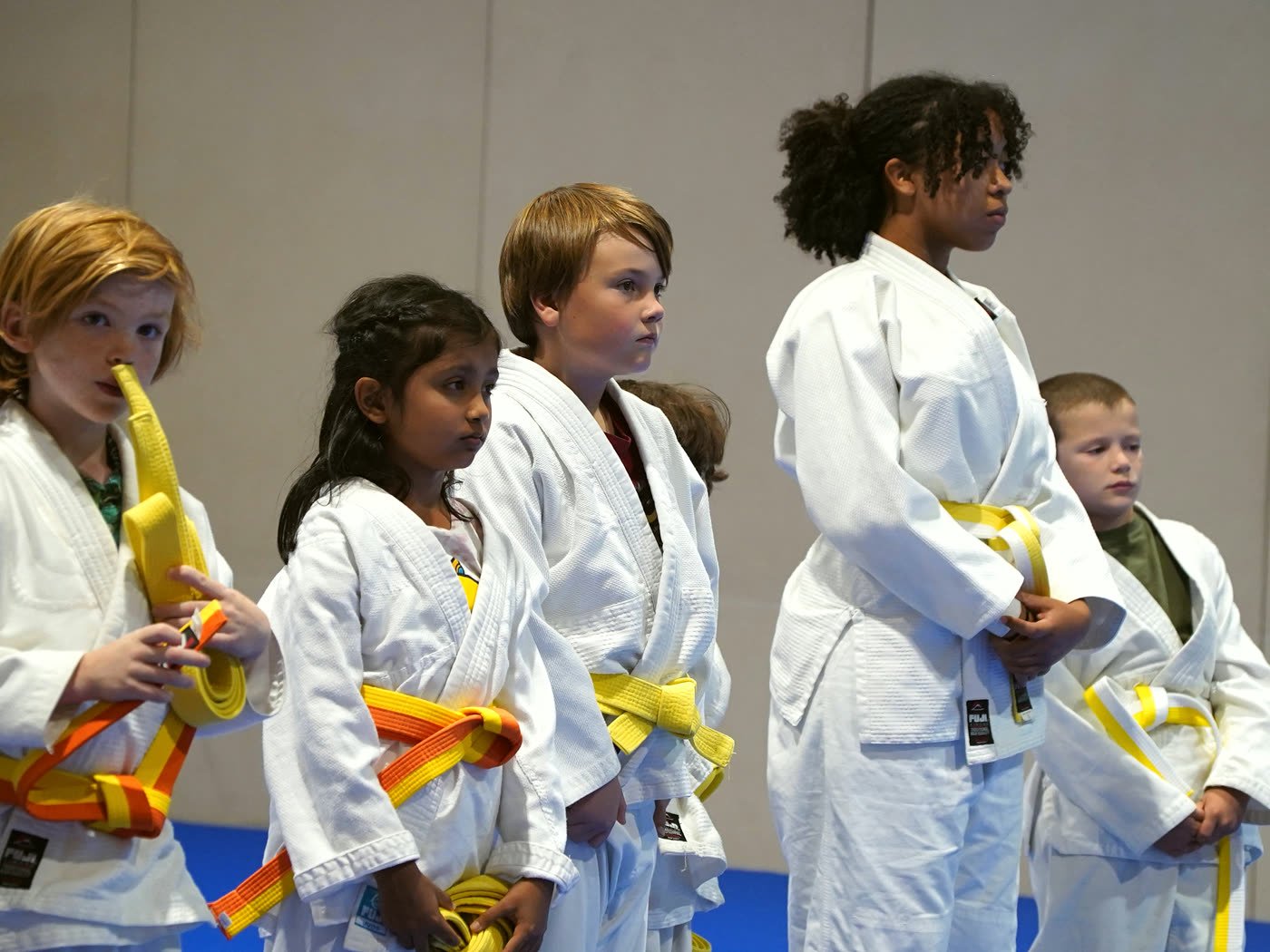 A line of students holding their new belts, one playfully chewing his