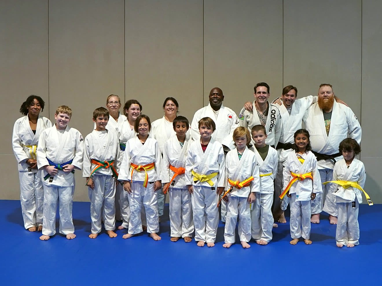 Shining Together Judo students and coaches smiling together in their judogi on the blue mats